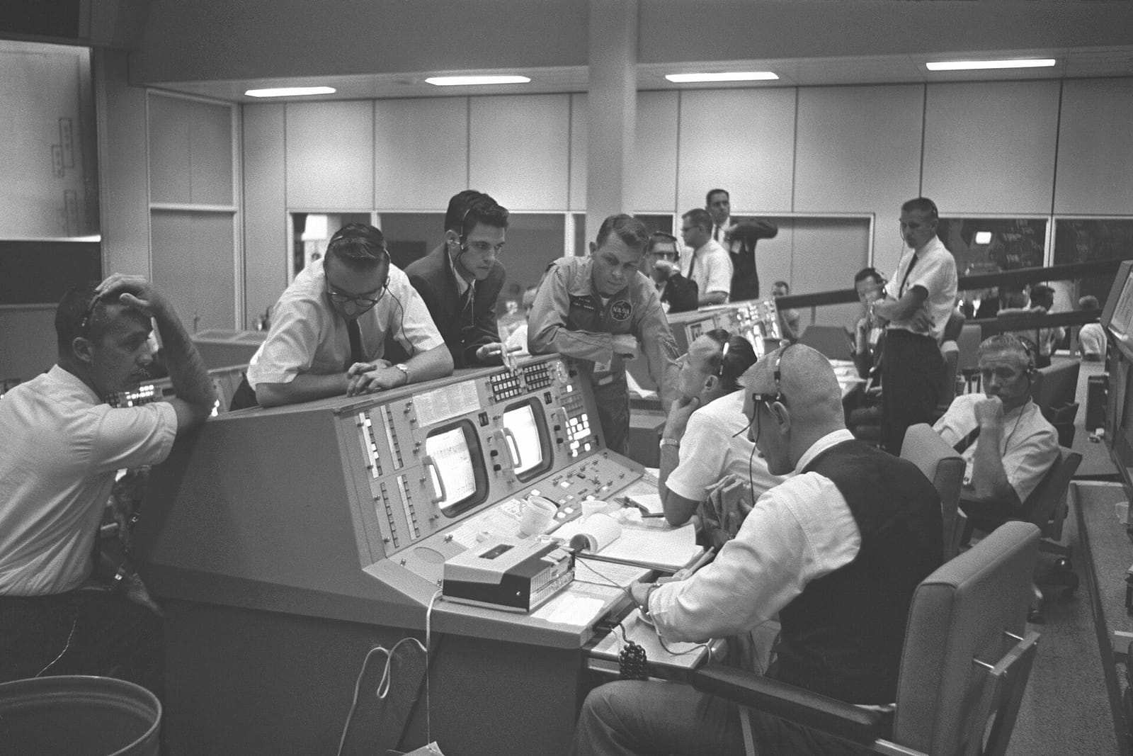 Vue d’ensemble de la salle de contrôle de mission, avec ses pupitres, ses écrans et les contrôleurs de vol penchés sur leurs consoles.
